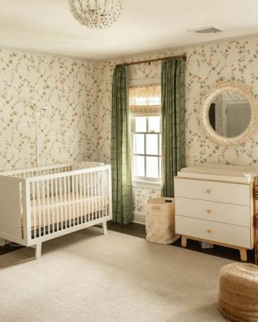 bērnudārzs, ziedu tapetes, zaļi aizkari, balta gultiņa, balta un koka kumode, plikas zonas paklājs