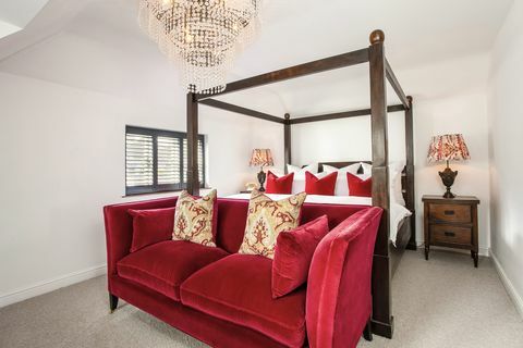 balta guļamistaba ar gultu ar baldahīnu un sarkanu dīvānu