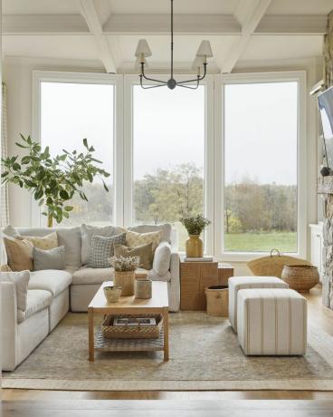 dzīvojamā istaba ar logiem no grīdas līdz griestiem ar skatu uz zaļu lauku
