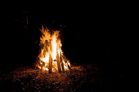āra ugunskurs ar augstām liesmām, kas atrodas dēļos, kas veidoti kā teepee
