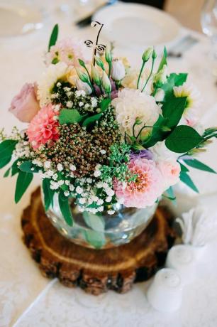Kāzu galda ziedu dekorēšana. Stikla vāze ar galda numuru viesiem ar apstādījumiem, rozēm, lisianthus un citiem ziediem.