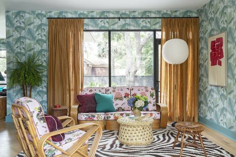 dzīvojamā istaba ar zebras zonas paklāju, palmu tapetes, oranži aizkari uz melniem aizkaru stieņiem, rozā tropu dīvāns