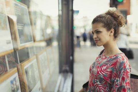 Jauna sieviete, pārlūkojot nekustamo īpašumu sarakstus pie pilsētas veikalu