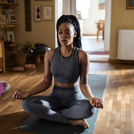 melna sieviete, kas sēž saulainā istabā, meditē lotosa pozā