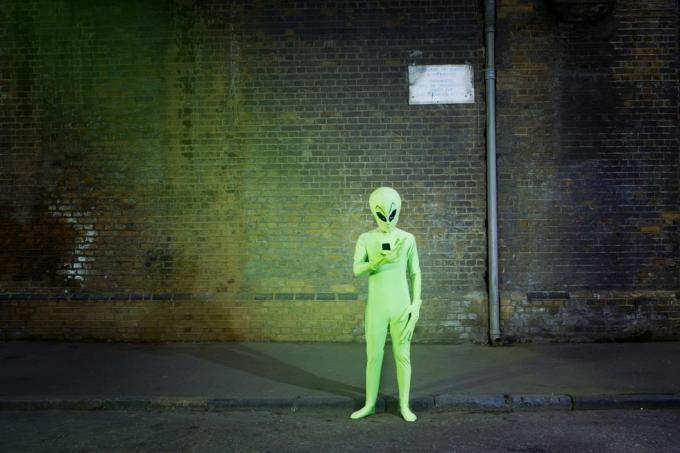 vīrietis, ģērbies citplanētiešu kostīmā, skatās uz mobilo tālruni