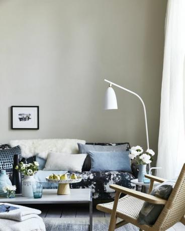 neitrāla viesistaba, viesistaba ar spilveniem uz zila raksta dīvāna, saliekta balta stāvlampa virs dīvāna pilieni, plankumi un izšļakstījumi rada mūsdienīgu impresionistisku izskatu un atslāba