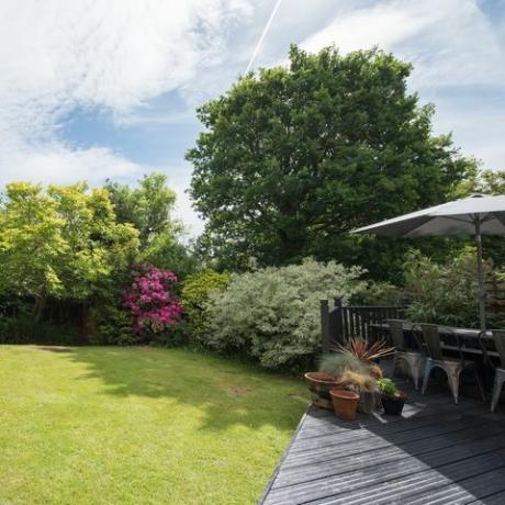 vispārējs skats uz aizmugurējo dārzu ar pelēku ieklāšanas zonu ar dārza galdu un krēsliem saulainā dienā mājās
